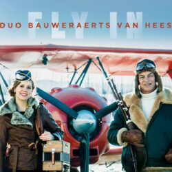 Duo Bauweaerts Van Hees gekleed in retro vliegeniers outfit voor een oude rode vliegtuig
