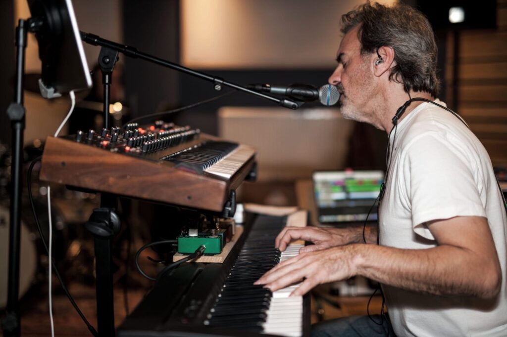 Een foto van muzikant stefan van puymbroeck zitten achter een dubbel elektrische piano en microfoon.