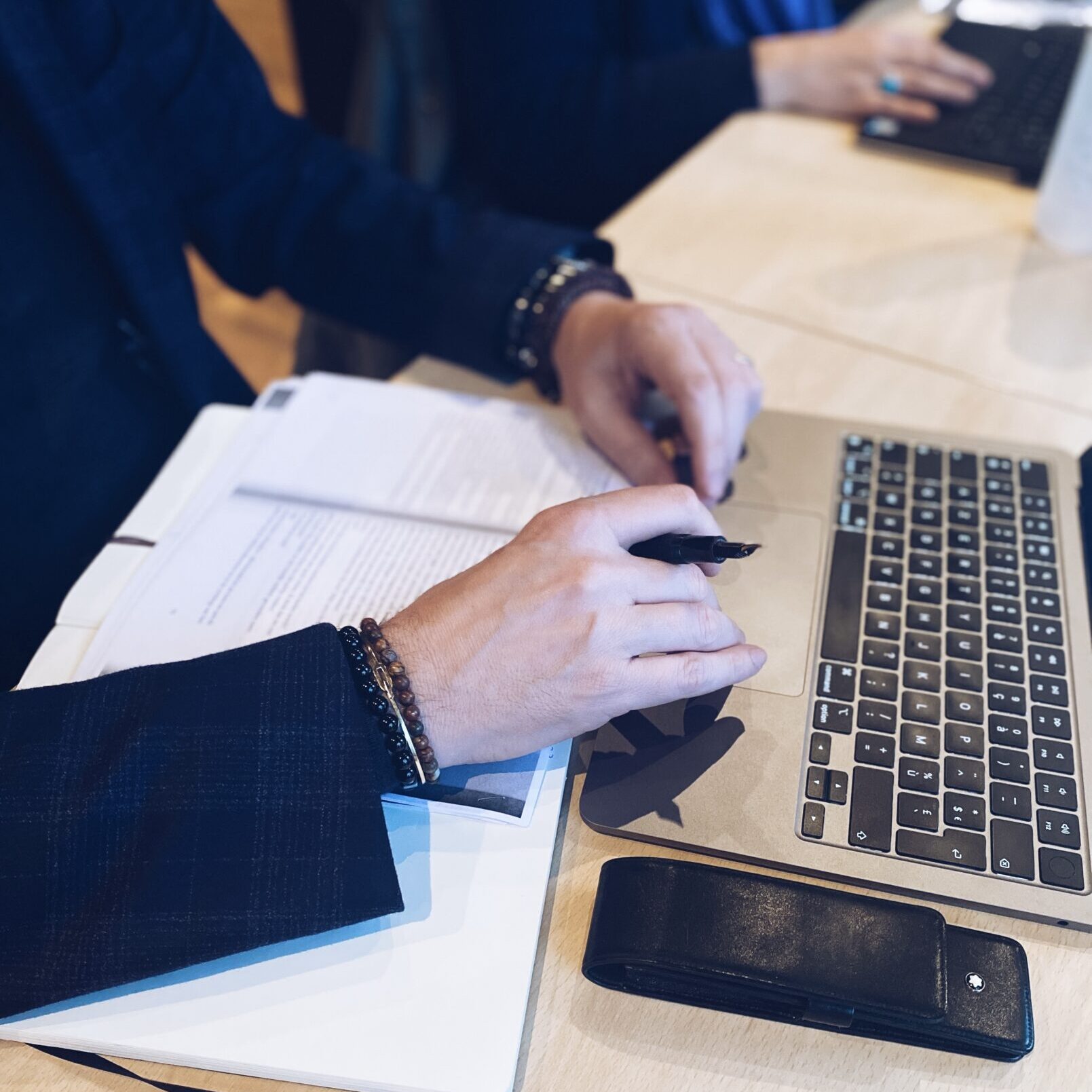 lose-up-handen met pen boven een toetsenbord daarnaast een stapenlteksten op papier