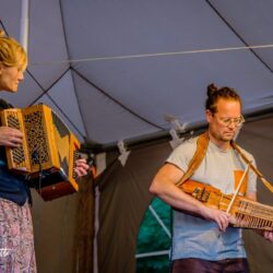 foto van het duo op en overdekt podium links vrouw met accordeon, rechts man met nyckelharpa